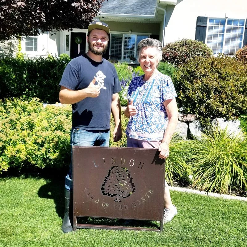 Happy Lindon homeowners with Yard of the Month sign on a lush green lawn